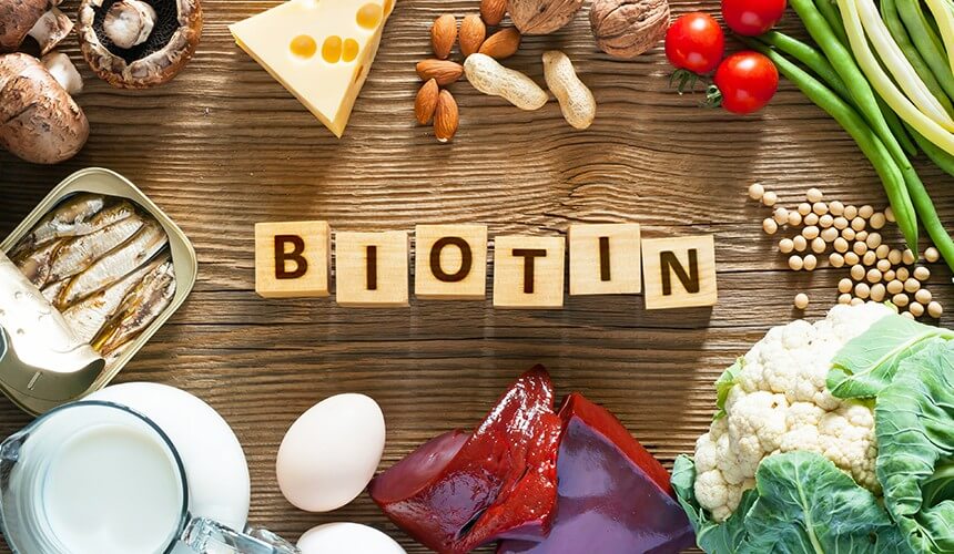 Biotinová cedule z dřevěných kostek na dřevěném stole, potraviny bohaté na biotin v okolí