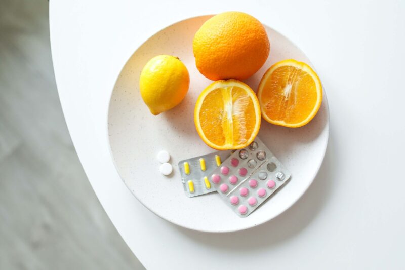 Rozkrojený a celý pomeranč na bílém talíři na stole a na něm různé léky.
