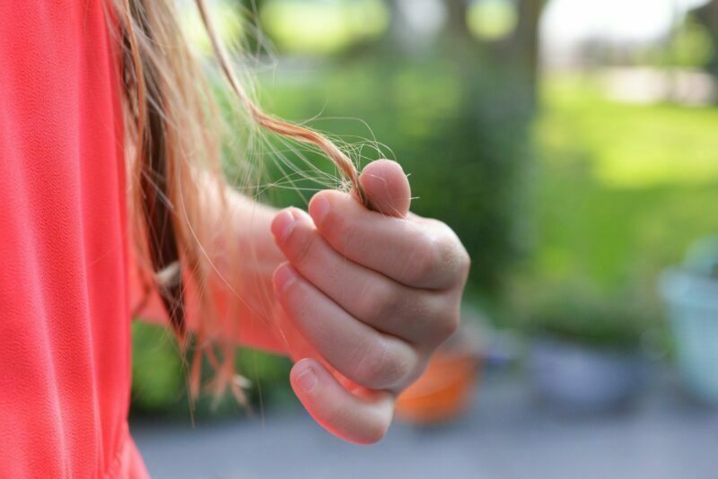 Žena si drží konečky vlasů prsty, v pozadí zeleň